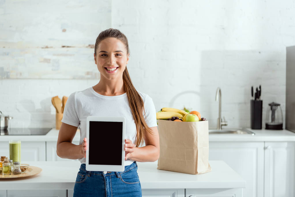 счастливая девушка держит цифровой планшет с чистым экраном рядом с продуктами
  - Фото, изображение