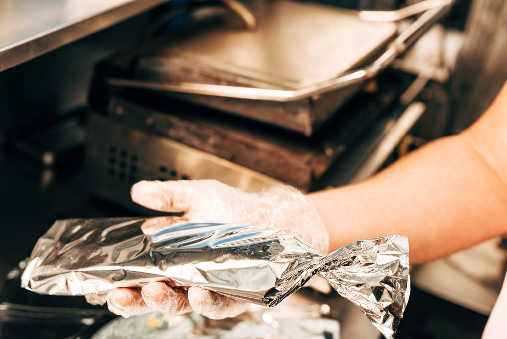 cropped view of cook in glove holding doner kebab in aluminium foil - Photo, Image
