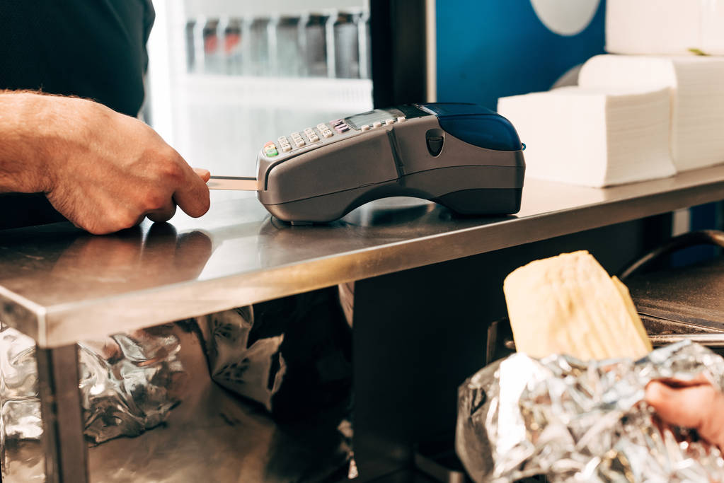 обрізаний вид чоловіка, який купує шашлик донора в алюмінієвій фользі та касирі, використовуючи платіжний термінал
 - Фото, зображення