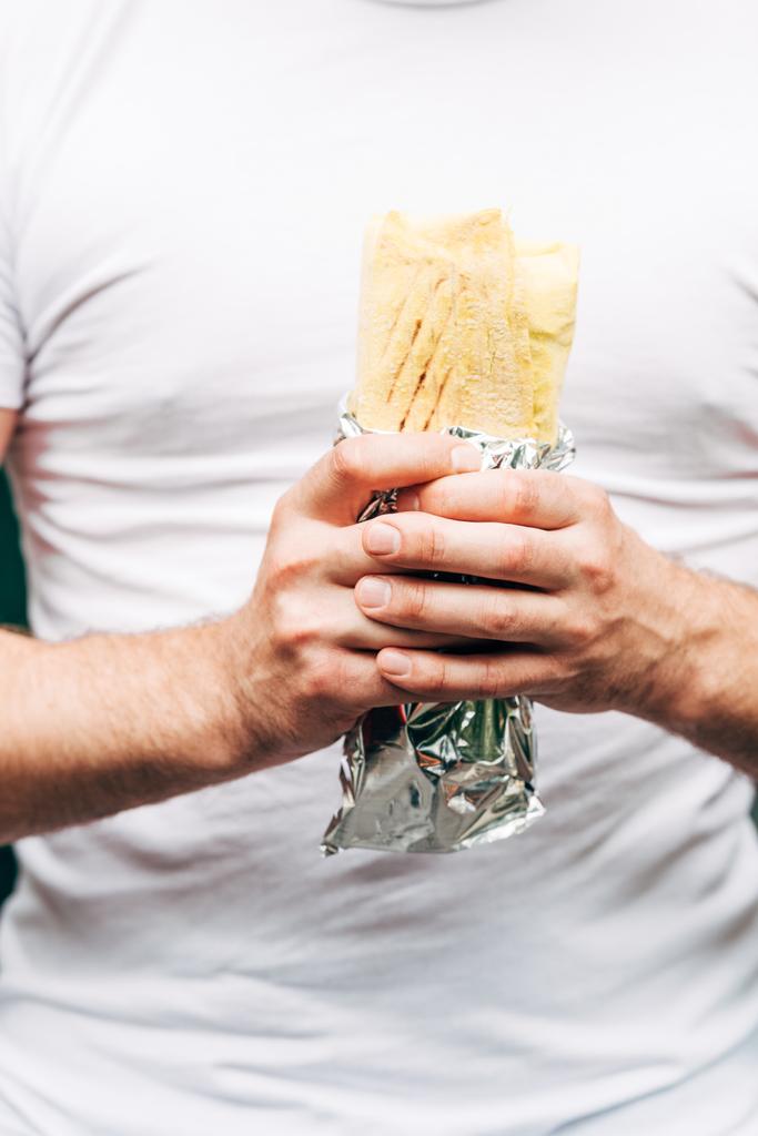 částečný pohled na muže držící kebabu kebab v hliníkové fólii - Fotografie, Obrázek