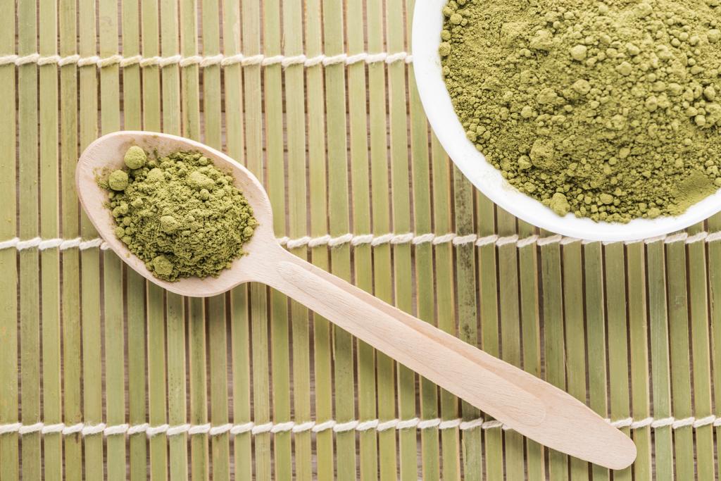 Widok z góry miskę i drewnianą łyżką z proszkiem zielonej herbaty Matcha na mat bambusa - Zdjęcie, obraz