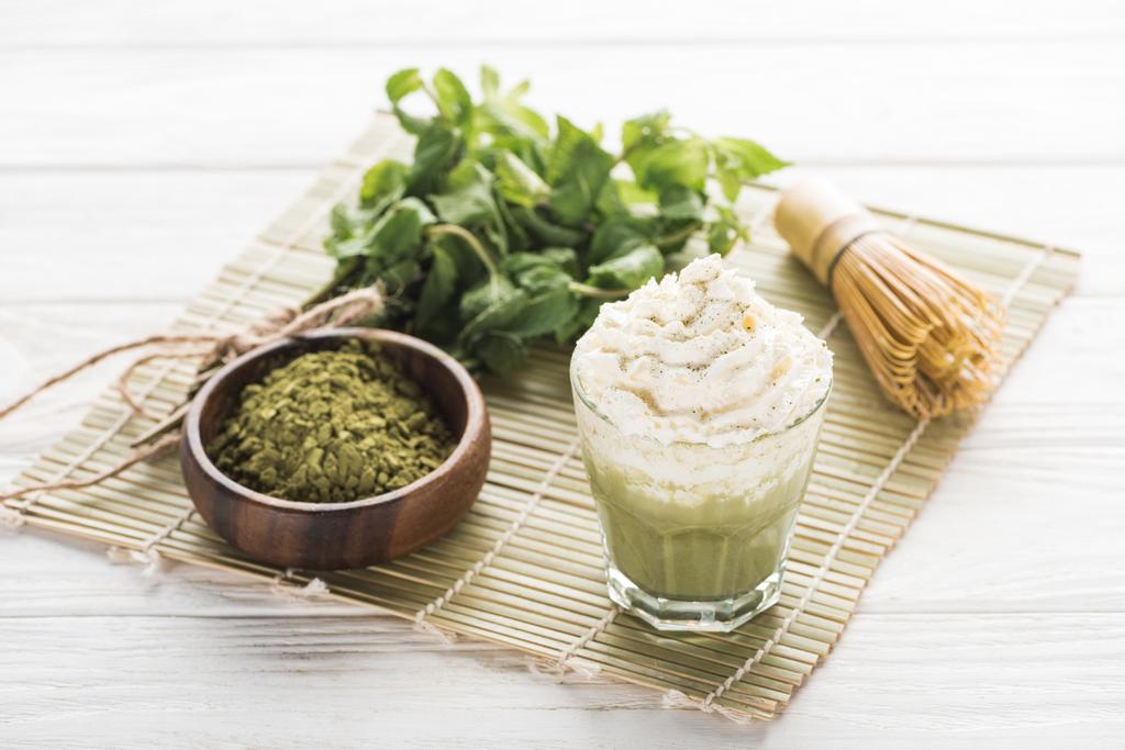 Matcha grüner Tee mit Schlagsahne auf Bambusmatte mit Pulver, Minze und Schneebesen - Foto, Bild