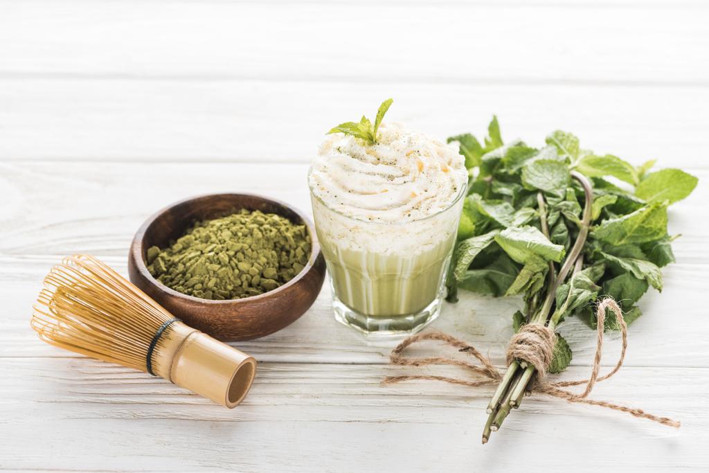 verre de thé vert matcha avec crème fouettée sur table blanche avec poudre, menthe et fouet
 - Photo, image