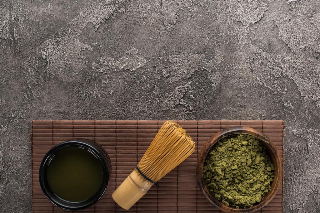 Top uitzicht op groene Matcha thee met garde op bamboe mat op donkere stenen tafel - Foto, afbeelding