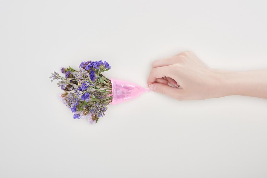 cropped view of woman holding plastic menstrual cup with wildflowers isolated on grey - Photo, Image