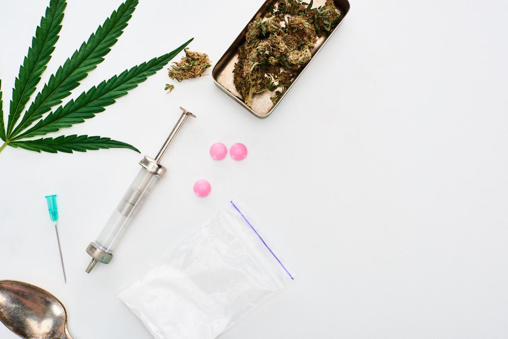 Widok z góry na pąki marihuany, liść konopi, łyżka, heroina, LSD i strzykawki na białym tle - Zdjęcie, obraz