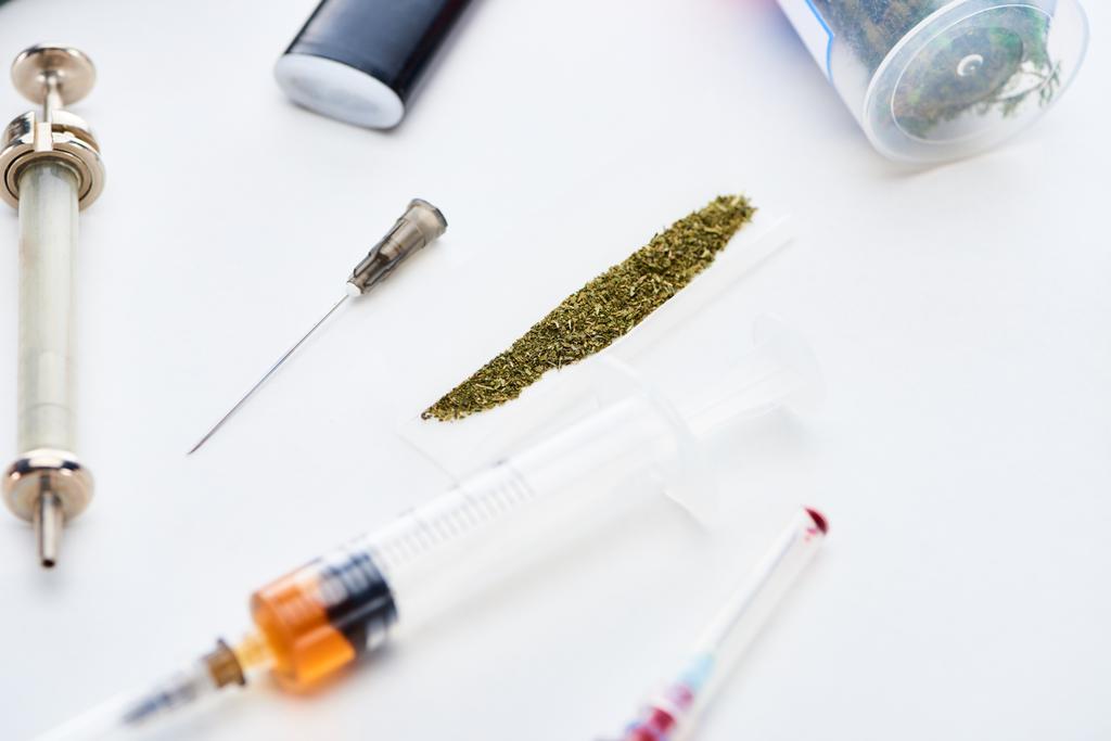 селективный фокус шприцов рядом с бумагой с марихуаной на белом фоне
 - Фото, изображение