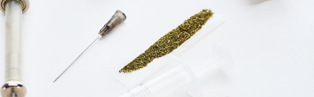 enfoque selectivo de jeringas cerca de papel de liar con marihuana sobre fondo blanco, plano panorámico
 - Foto, imagen