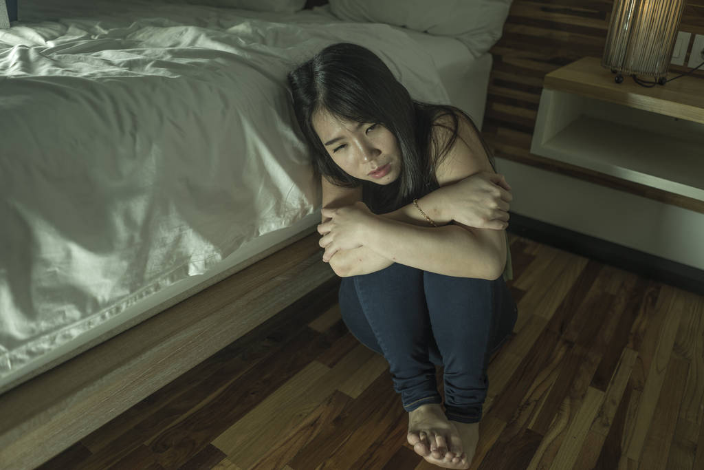  若い落ち込みと悲しいアジアの日本人女性は、うつ病の問題と不安の危機感に苦しんでベッドの隣の寝室の床に座って絶望的な感じ - 写真・画像
