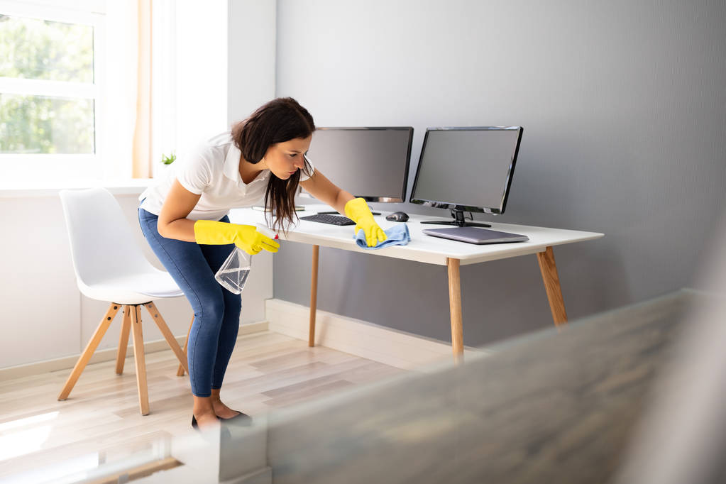 Widok z boku kobiety Janitor sprzątanie biurko z niebieskim serwetki w biurze - Zdjęcie, obraz