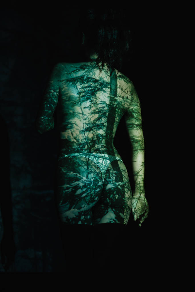 Вид сзади раздетой девушки с тенями на теле, стоящей на черном
  - Фото, изображение
