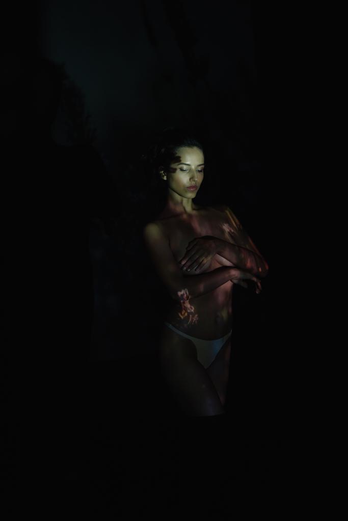 mladá žena s zavřenýma očima a stíny na těle stojící na černém  - Fotografie, Obrázek