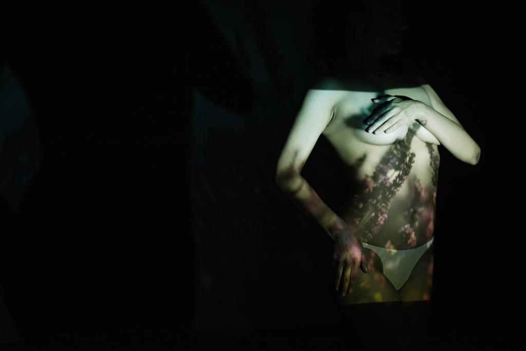 Mädchen bedeckt Brüste im Stehen mit der Hand auf der Hüfte auf schwarz mit Schatten  - Foto, Bild