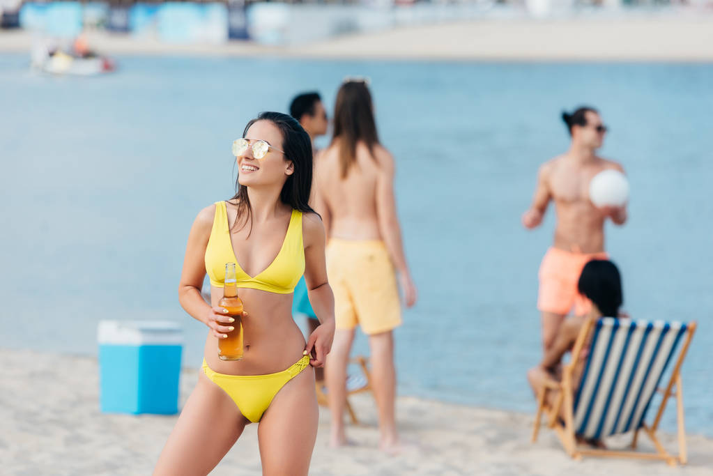 aantrekkelijke jonge vrouw in badpak op zoek weg terwijl staan op het strand  - Foto, afbeelding