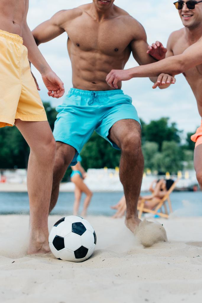 частичный взгляд молодых мультикультурных друзей, играющих в футбол на пляже
 - Фото, изображение