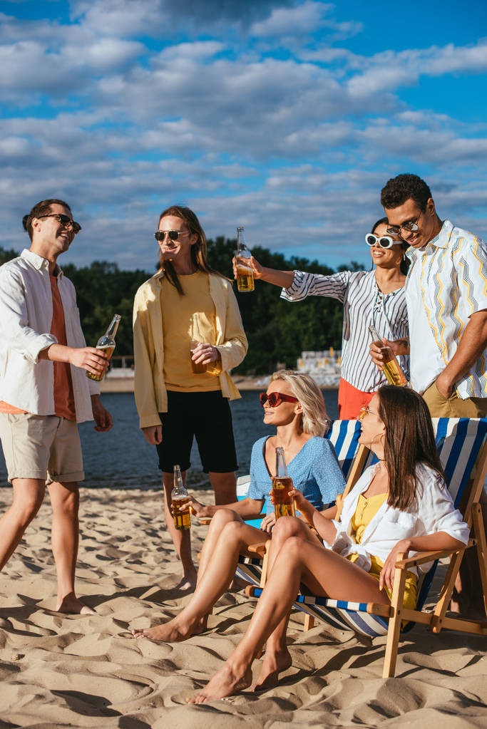 χαρούμενοι πολυπολιτισμικοί φίλοι μιλούν πίνοντας μπύρα στην παραλία - Φωτογραφία, εικόνα