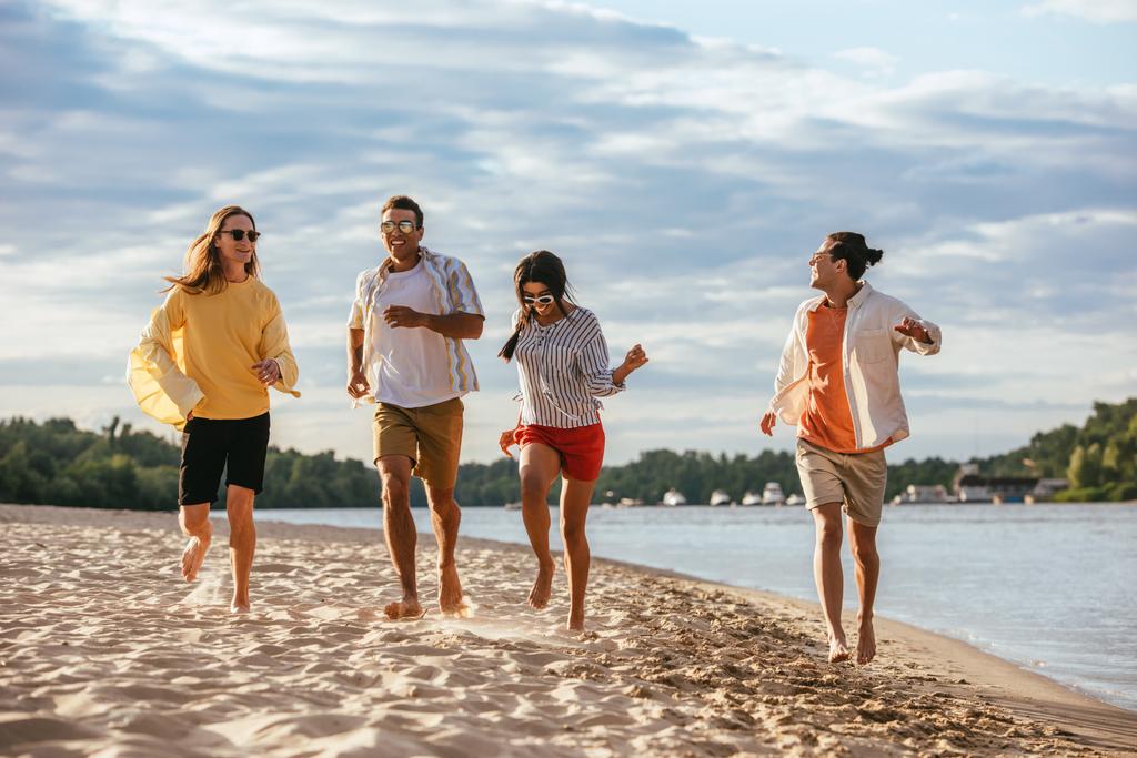 vidám multikulturális barátok futó homokos strand közelében folyó - Fotó, kép