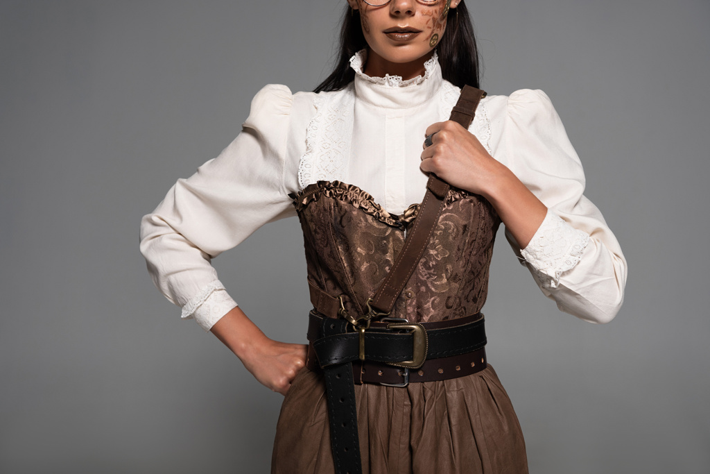 cropped view of steampunk woman with makeup standing with hand on hip isolated on grey - Photo, Image