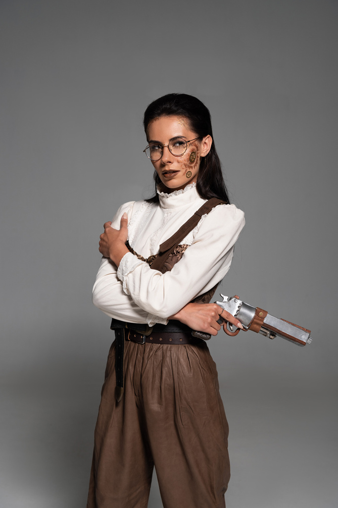 mujer steampunk pensativa en gafas con pistola y mirando hacia otro lado en gris
 - Foto, imagen