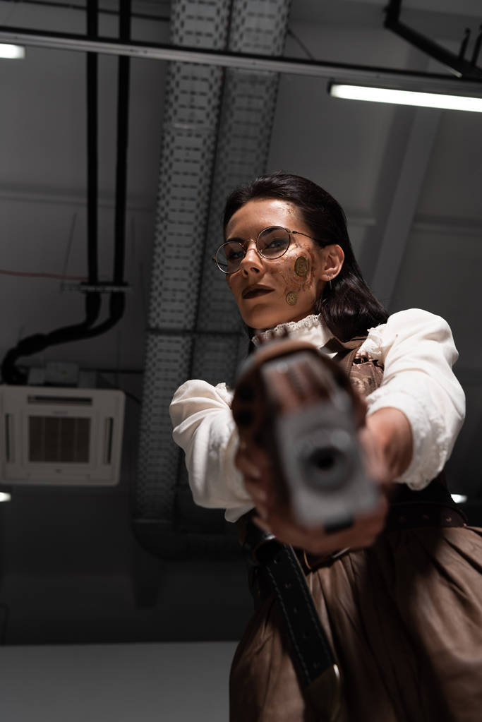 selectieve focus van vertrouwen Steampunk vrouw richten met pistool op camera - Foto, afbeelding