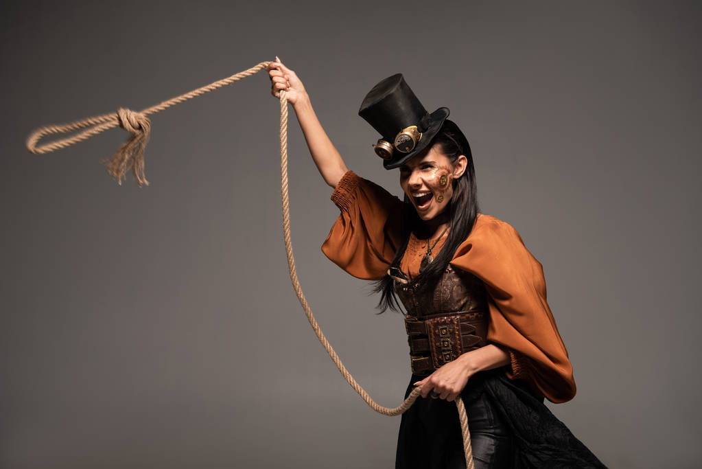 attractive steampunk girl in top hat holding lasso and screaming isolated on grey - Photo, Image