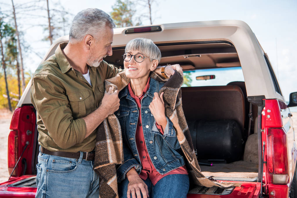 sorridente coppia anziana seduta in auto con coperta e guardarsi l'un l'altro
 - Foto, immagini