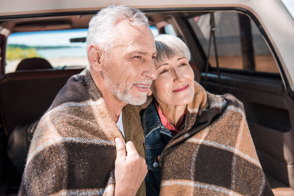 battaniye ile arabada oturan gülümseyen yaşlı çift - Fotoğraf, Görsel