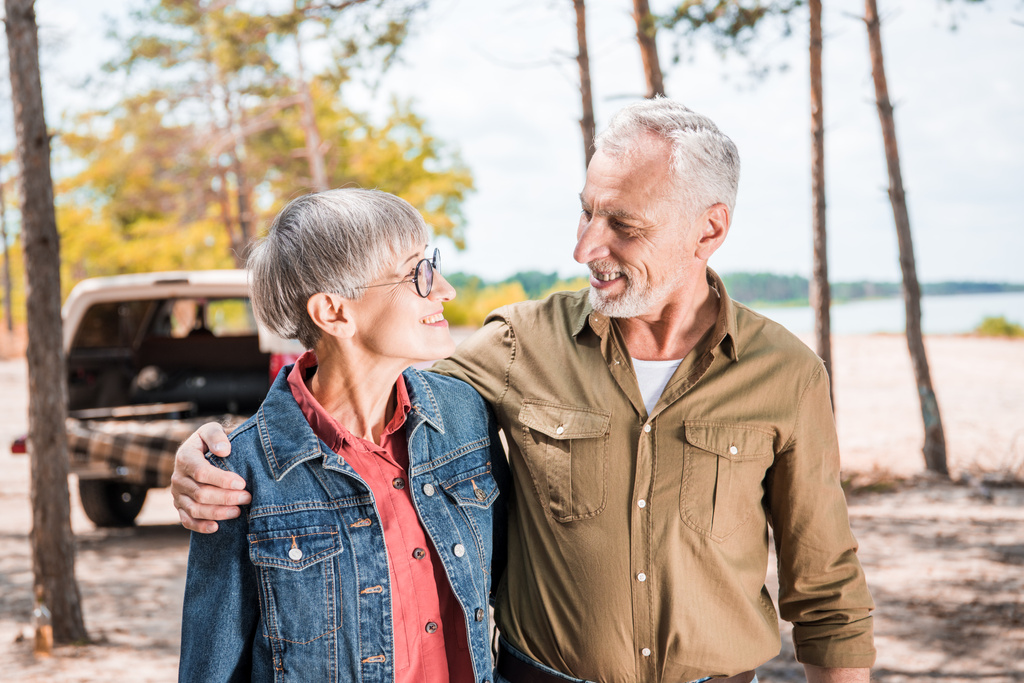 glückliches Senioren-Paar umarmt und sieht einander im Wald an einem sonnigen Tag an - Foto, Bild