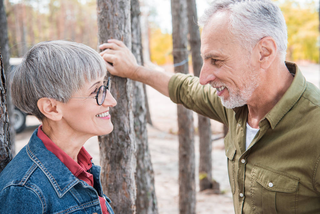 Glückliches Seniorenpaar schaut einander an und lächelt im Wald - Foto, Bild