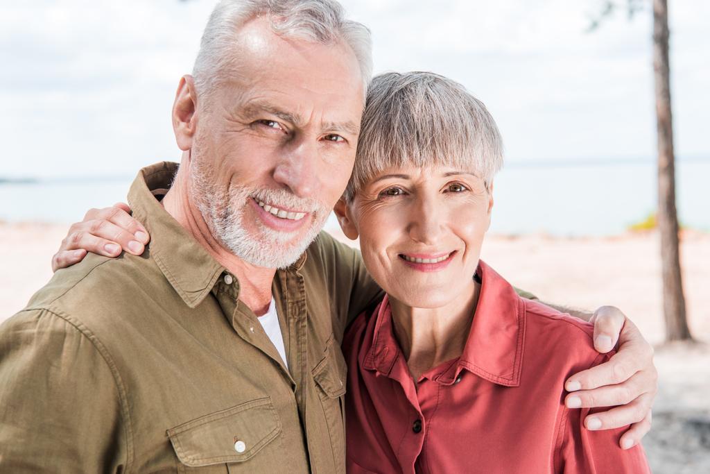 mutlu yaşlı çift kucaklayan ve plajda gülümseyen - Fotoğraf, Görsel