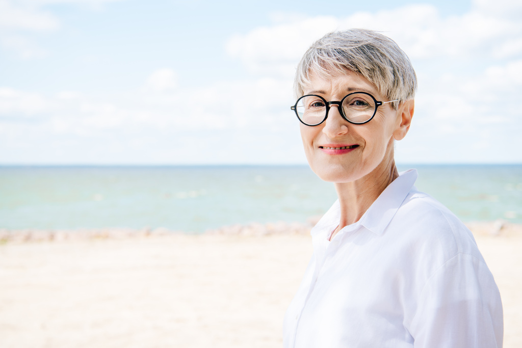 donna anziana sorridente in occhiali e camicia bianca guardando la fotocamera in spiaggia
 - Foto, immagini