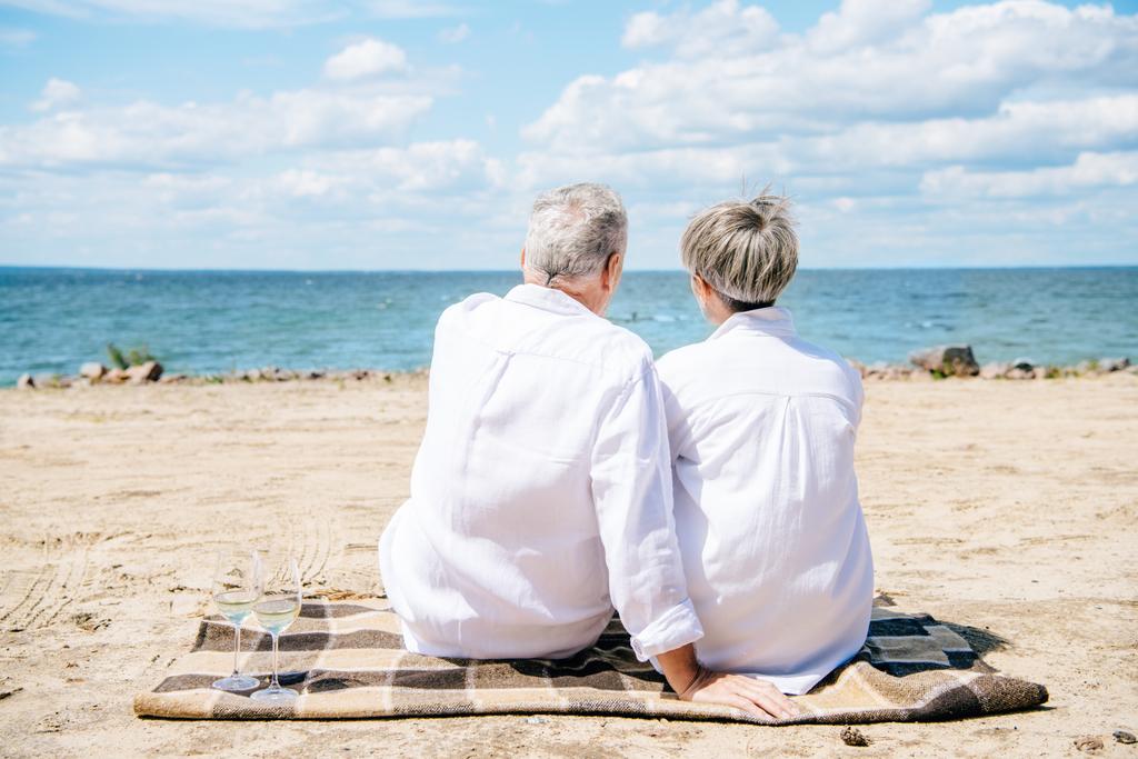vue arrière du couple aîné en chemises blanches assis sur la couverture à la plage
 - Photo, image