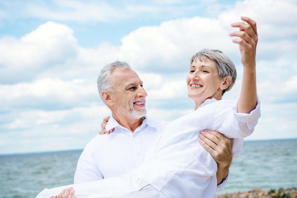 uomo anziano sorridente in camicia bianca moglie tenuta sotto il cielo blu vicino al fiume
 - Foto, immagini