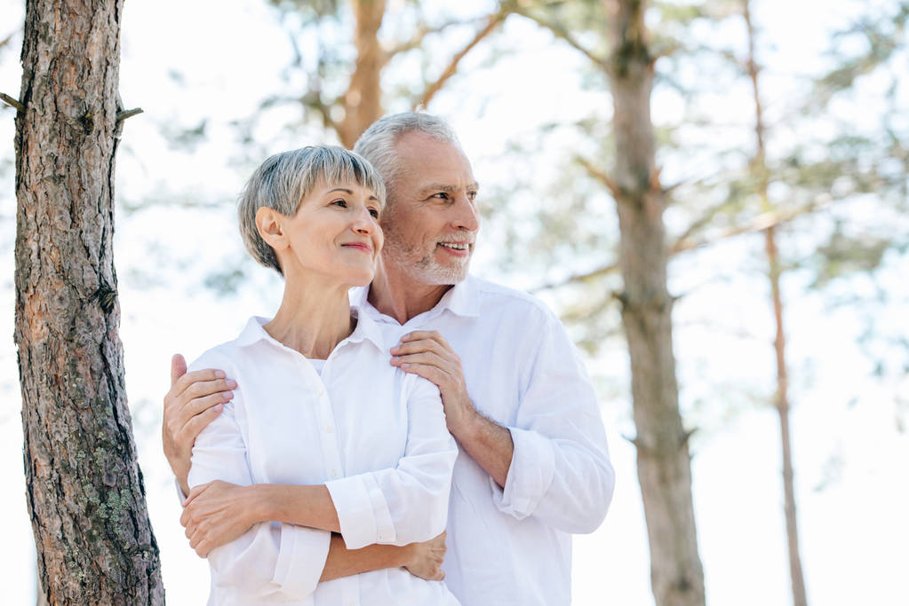 sourire couple aîné en chemises blanches embrassant et regardant loin dans la forêt
 - Photo, image