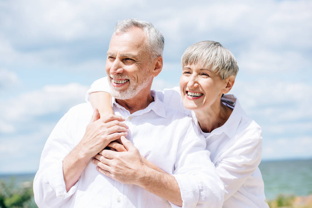 happy senior couple in white shirts embracing under blue sky - Photo, Image