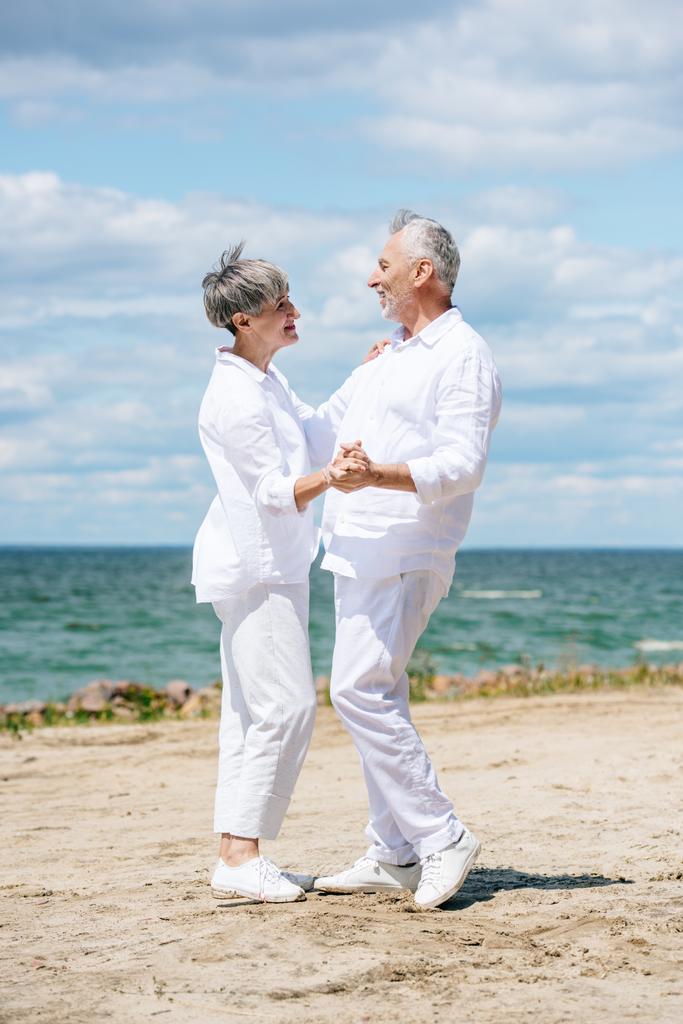 teljes hosszúságú tekintettel boldog Senior pár nézi egymást, miközben táncolnak a strandon - Fotó, kép
