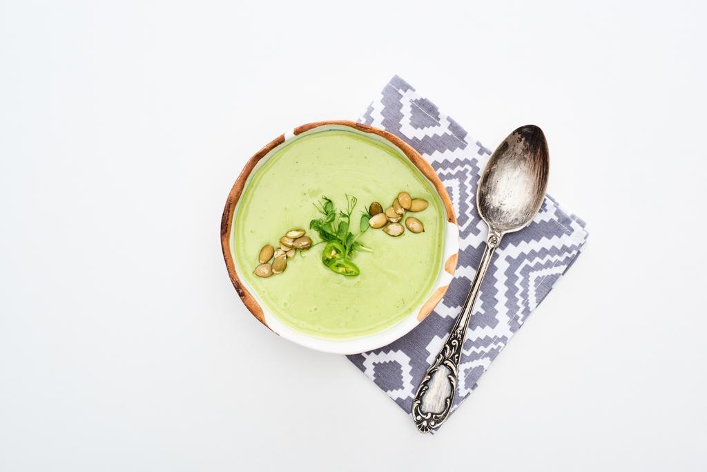 vista superior de la deliciosa sopa de verduras verde cremosa con brotes y semillas de calabaza en la servilleta con cuchara aislada en blanco
 - Foto, Imagen