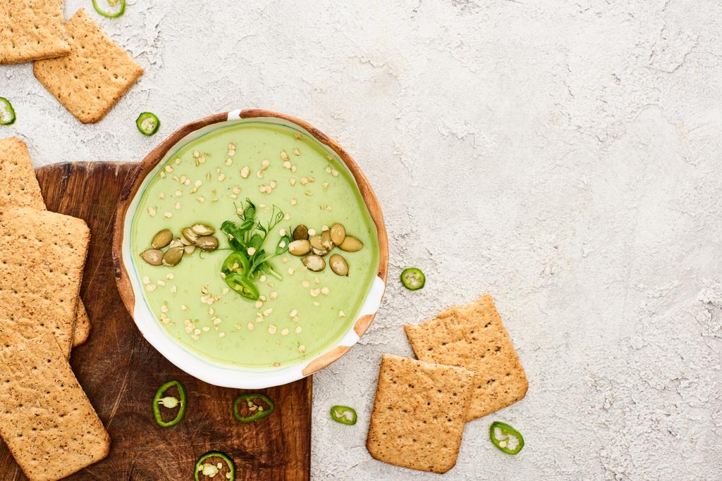 Blick von oben auf leckere grüne cremige Suppe mit Crackern auf Holzhackbrett - Foto, Bild