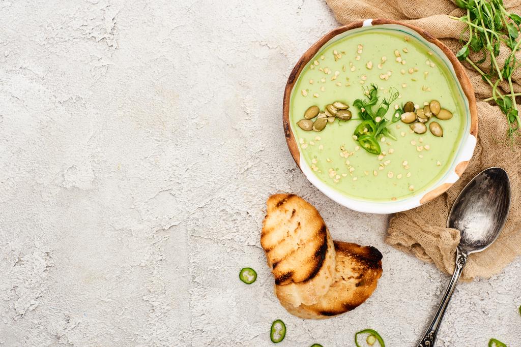 Widok z góry na smaczny zielony kremowy zupa z grzankami i kiełki na teksturowanej szarym tle z rustykalną szmatką - Zdjęcie, obraz