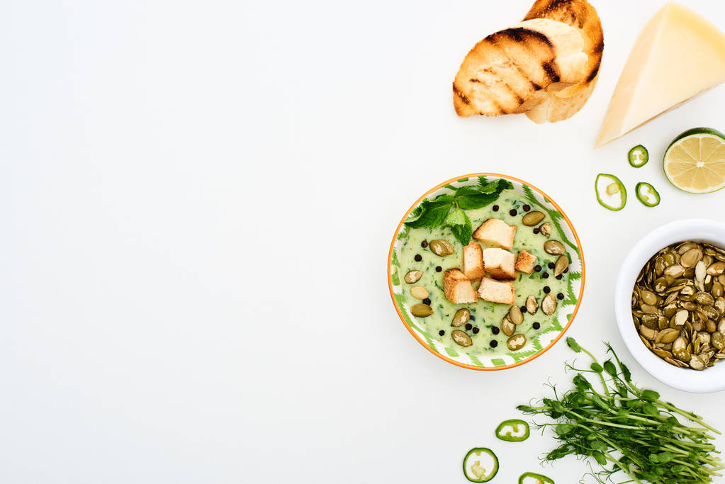 Widok z góry na pyszne kremowo-zielone zupy warzywne podawane z serem i grzankami na białym tle - Zdjęcie, obraz