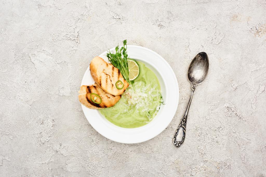 vista superior de la deliciosa sopa de verduras verde cremosa con croutons servidos con cuchara
 - Foto, Imagen