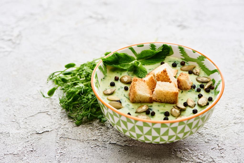 tál ízletes zöld zöldség tejszínes leves krutonokkal, bors és tökmag közelében zöld hajtások - Fotó, kép