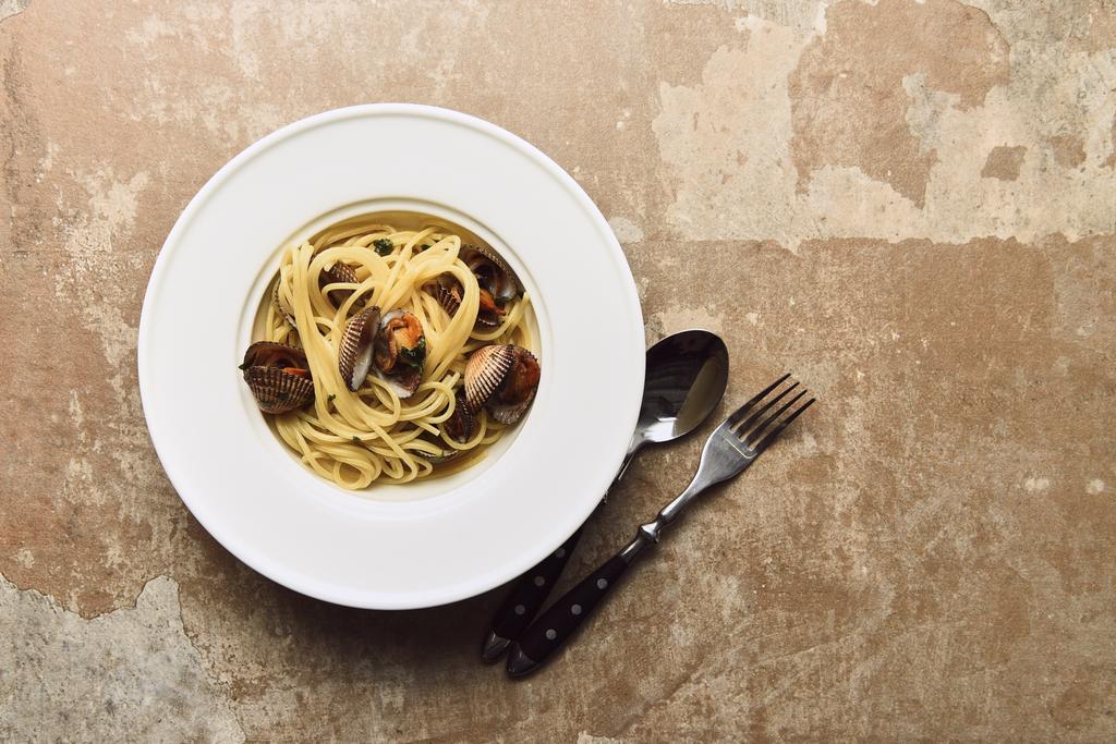vista dall'alto di deliziosa pasta con molluschi servita con cucchiaio e coltello su sfondo beige alterato
 - Foto, immagini