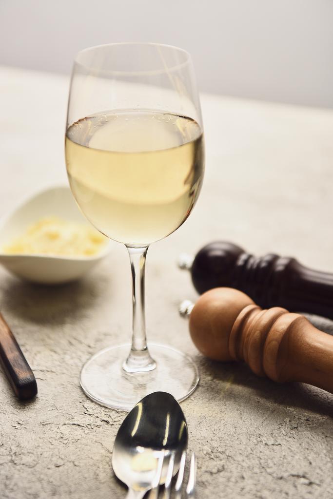 закрытый вид на стакан с белым вином рядом с перцово-солевыми мельницами и тертым сыром, изолированным на сером
 - Фото, изображение