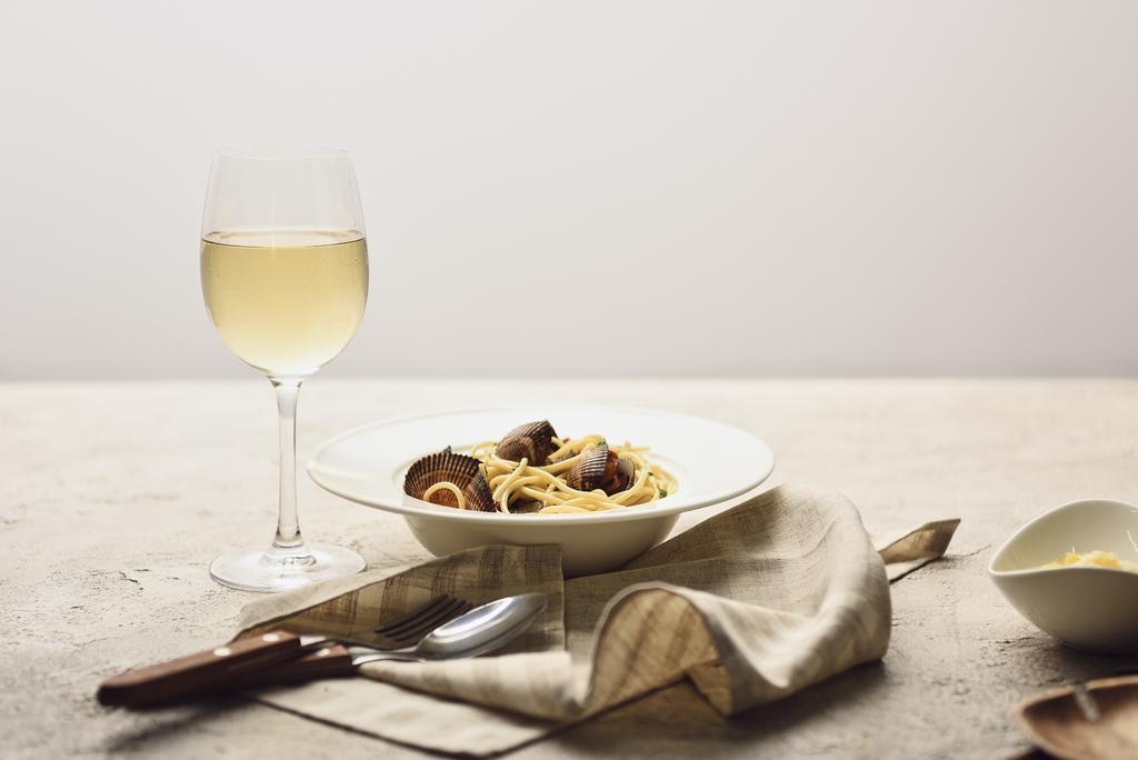 italienische Pasta mit Meeresfrüchten serviert mit Weißwein, Serviette und Besteck isoliert auf grau - Foto, Bild
