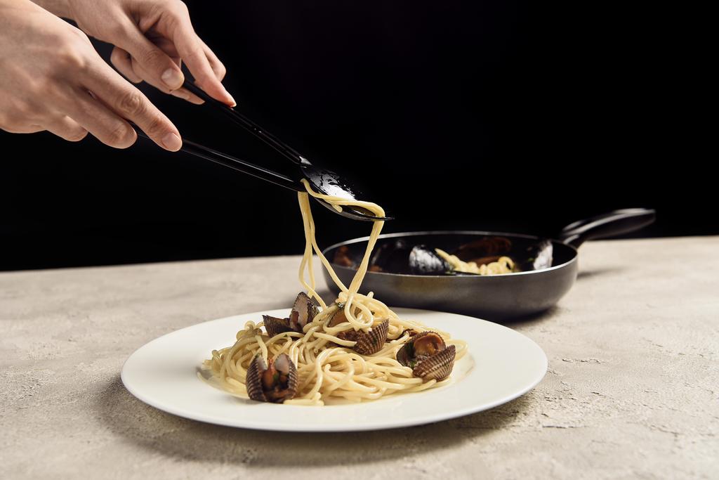 gedeeltelijke weergave van vrouw zetten heerlijke Italiaanse spaghetti met zeevruchten op plaat geïsoleerd op zwart - Foto, afbeelding