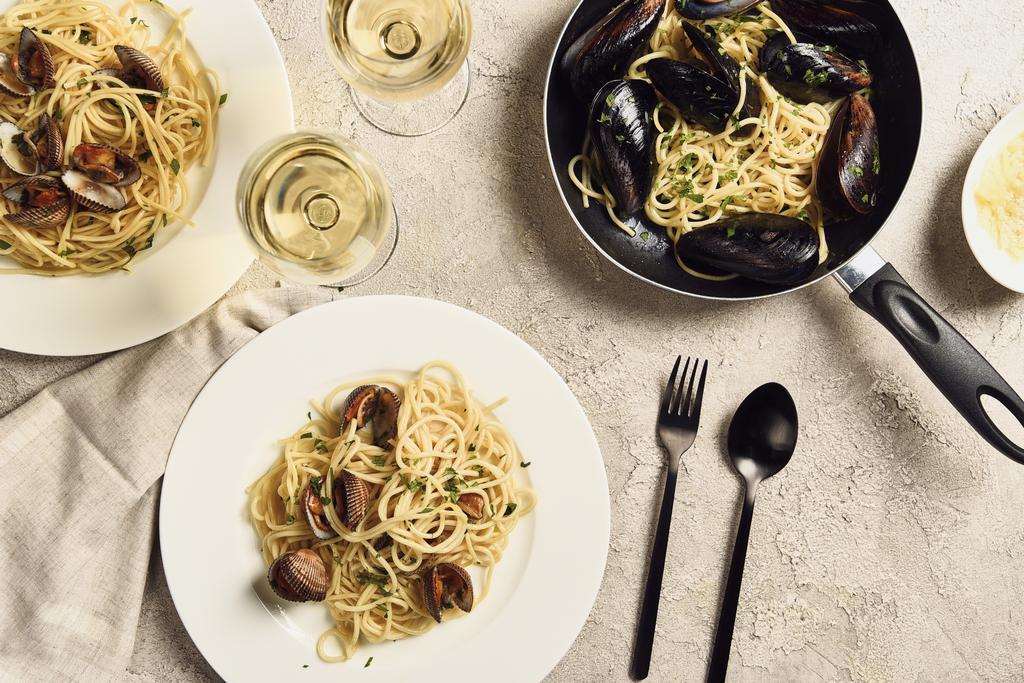 Top uitzicht op heerlijke pasta met zeevruchten geserveerd met witte wijn en servet op getextureerde grijs oppervlak - Foto, afbeelding