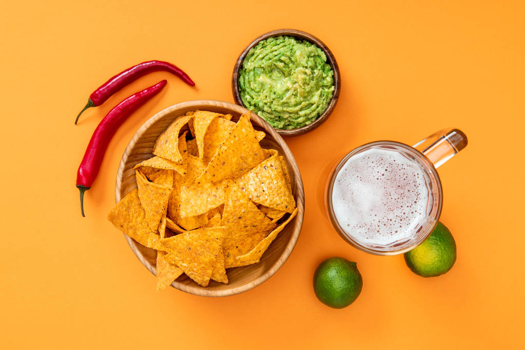top view of crispy nachos, guacamole, beer, limes and chili peppers on orange background, Mexican cuisine - Photo, Image