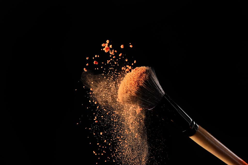 cepillo cosmético con polvo de naranja sobre fondo negro
 - Foto, Imagen