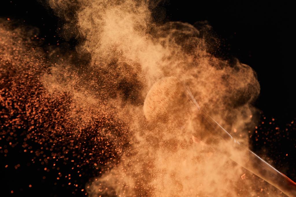 cepillo cosmético con colorida explosión de polvo naranja sobre fondo negro
 - Foto, imagen